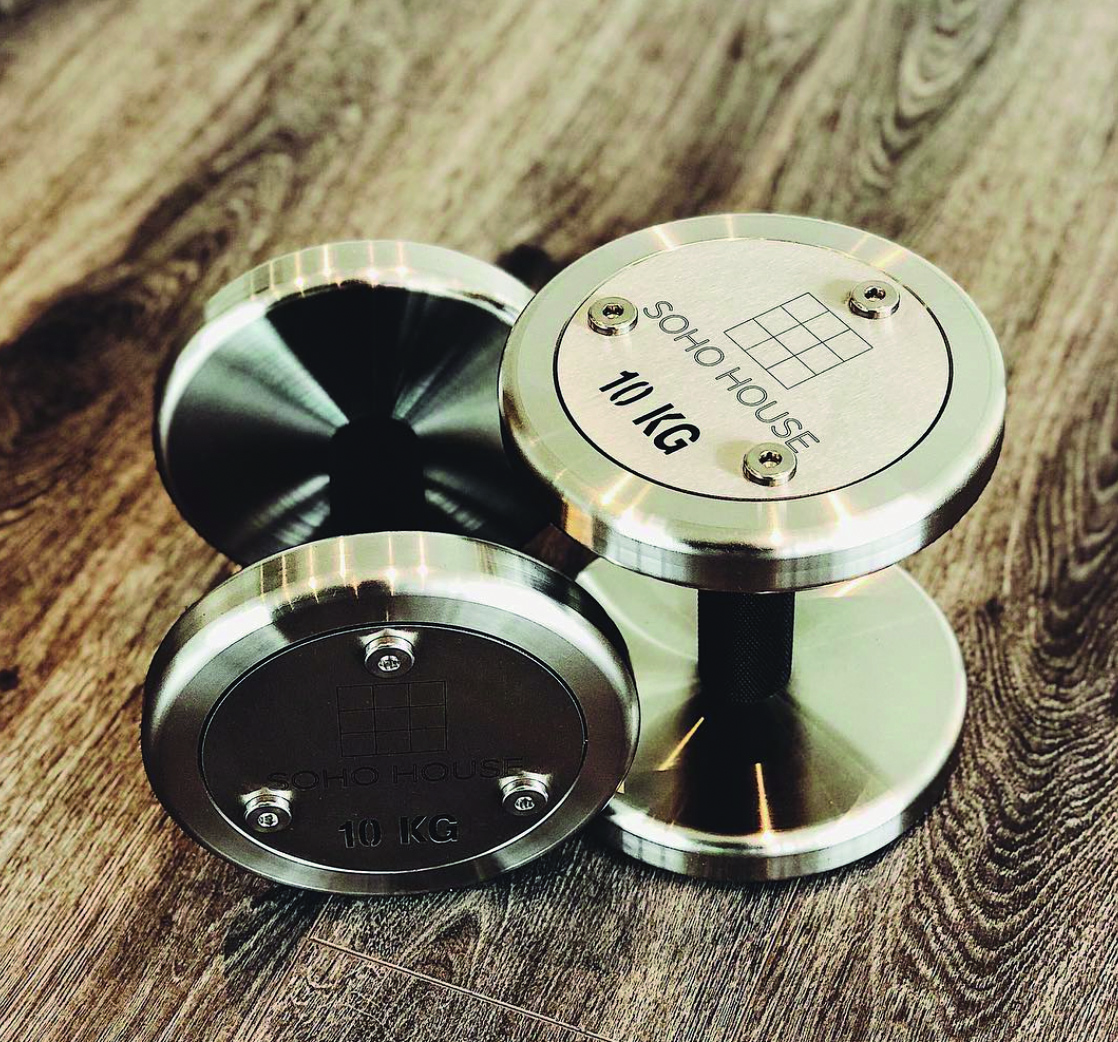 Branded chrome dumbbells with custom engraving on a walnut timber surface.