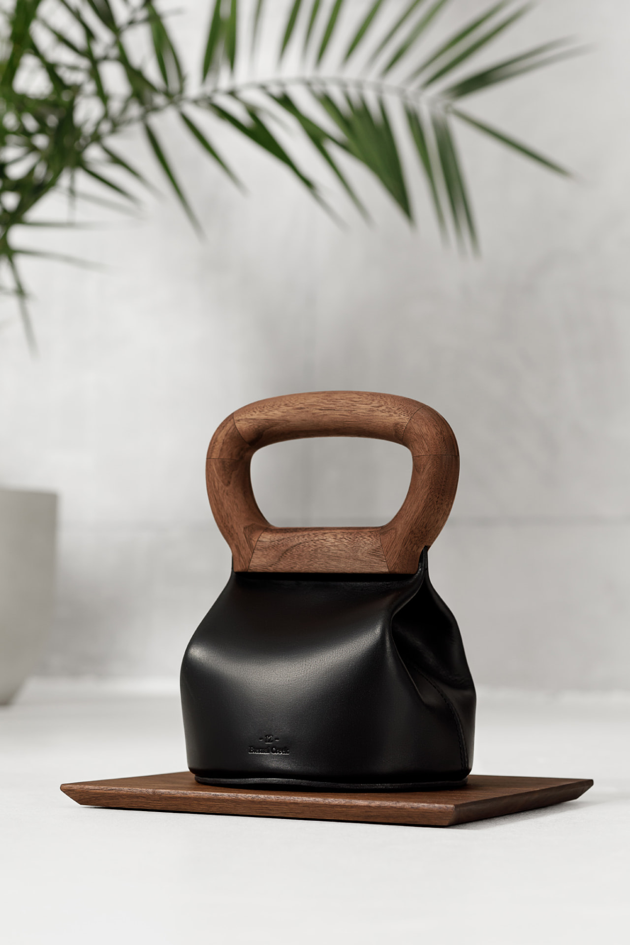 Black leather kettlebell with sculpted walnut handle and base, designed as a refined home gym accessory.