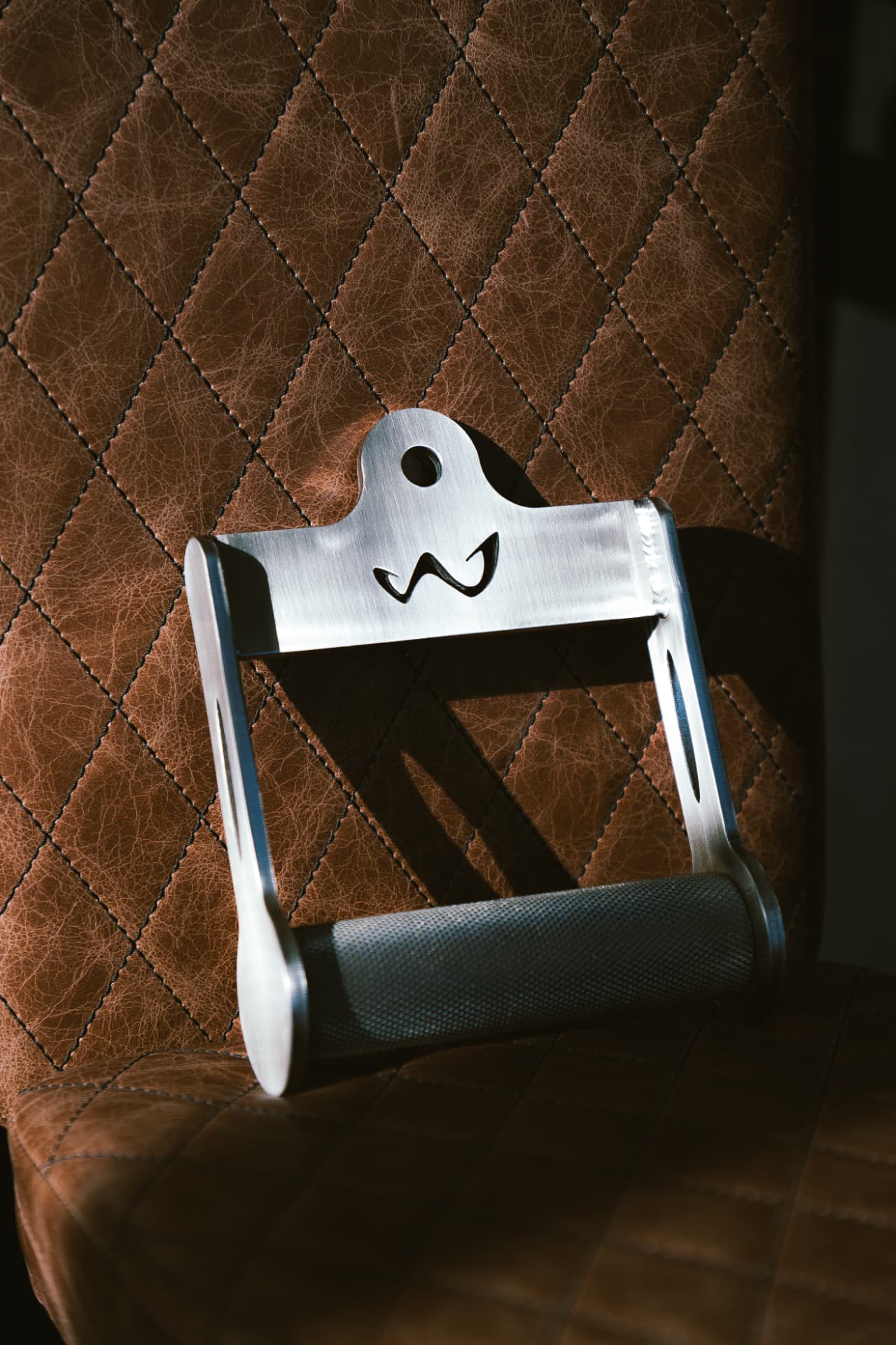 Custom Formance stainless steel handle with the studio monogram resting on quilted leather upholstery.